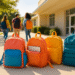 Colorful school backpacks for teens neatly arranged outside a school entrance, with students walking in the background on a sunny day.